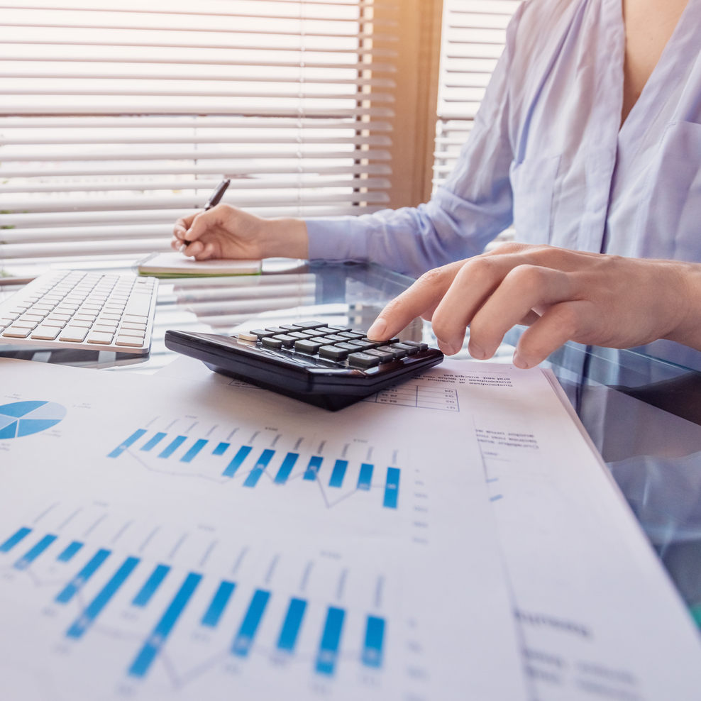 Businesswoman is sitting in front of a computer with calculator and pen. Printed diagrams are in the foreground.