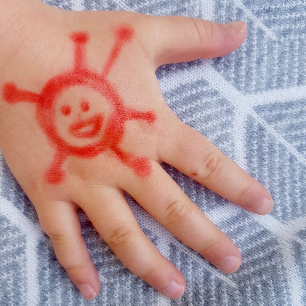 Kinderhand mit einem aufgemalten Coronavirus.