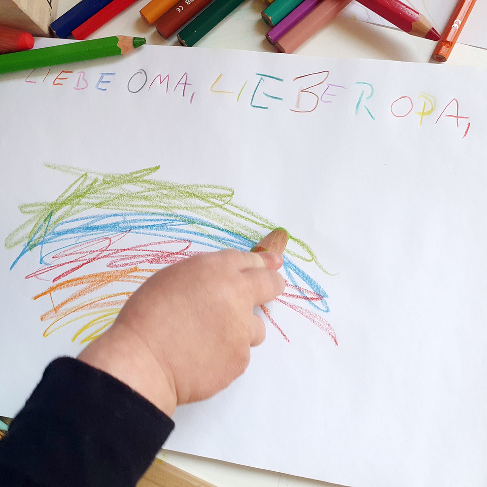 Child's hand with colored pencil paints a rainbow.